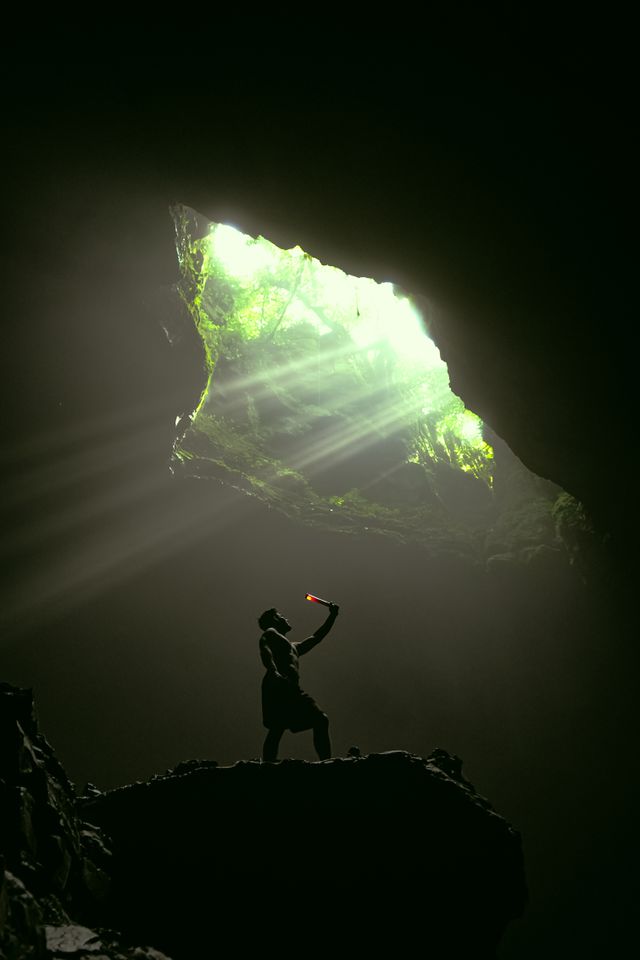 a man standing in front of a cave with light coming from the ground